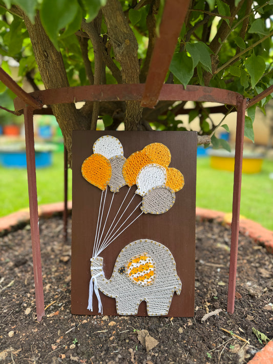 Decorative wall art of an elephant holding balloons in a garden setting